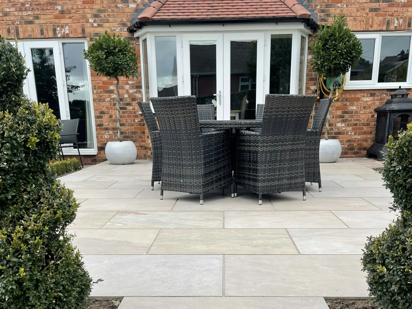 Terrasse mit hellen Steinplatten und Gartenmöbeln vor einem Haus